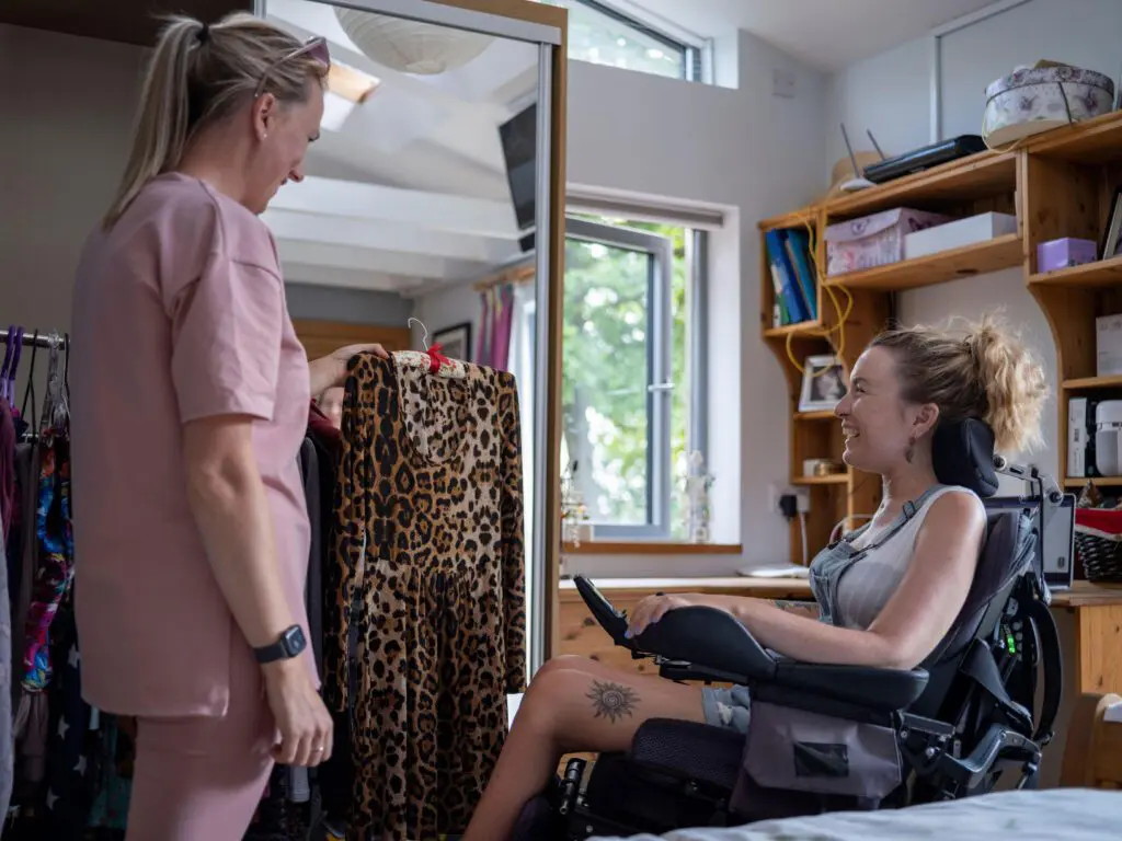 ADL-assistent in de gehandicaptenzorg helpt een vrouw in een rolstoel bij het kiezen van kleding